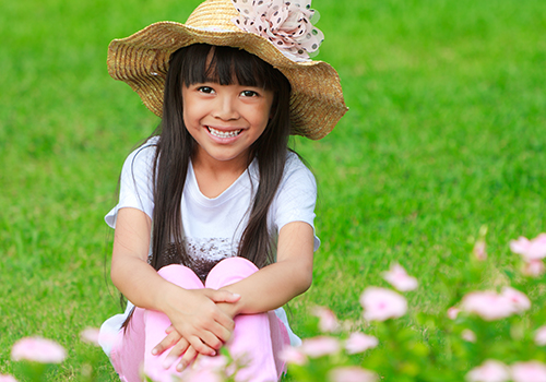 A little girl sitting on the grass wearing a hat.