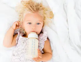 A baby girl laying in bed with her bottle.