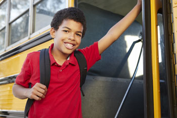 A boy with a backpack and school bag standing on the side of a bus.