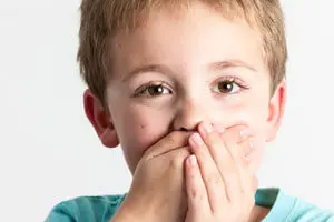 A young boy holding his hands to his mouth.
