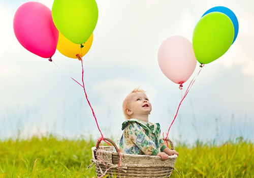 A baby sitting in a basket with balloons.
