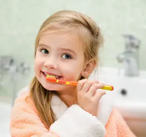 A little girl brushing her teeth with an orange toothbrush.