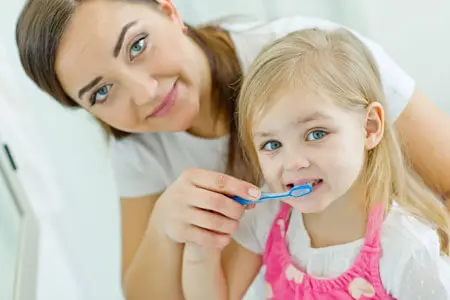 A woman and girl brushing their teeth together.