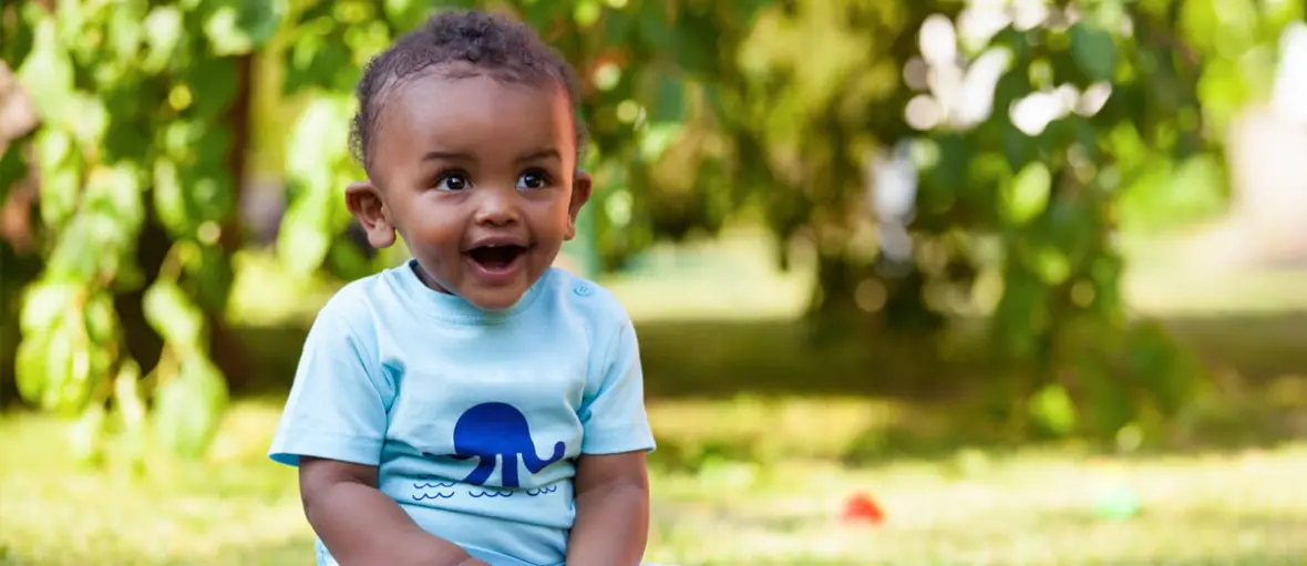 A baby boy wearing a blue shirt and smiling.